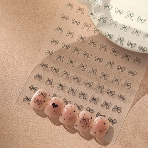 Détail de stickers nail art nœuds et cœurs noirs sur faux ongles roses translucides