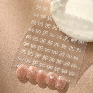 Détails de stickers nail art 3D avec nœuds blancs et motifs de cœurs sur ongles roses