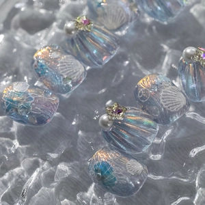 Close-up of iridescent blue press-on nails with shell texture, pearls, and star rhinestones