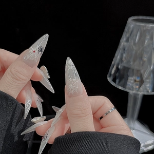 Detailed view of Halloween spider web stiletto press-on nails with red gems on black background