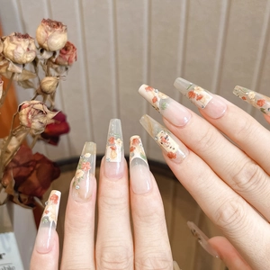 Detailed view of long coffin press-on nails with red floral patterns and crystal accents