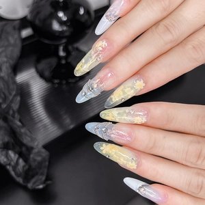 Détails d'ongles en amande avec fleurs jaunes, chaînes métalliques et strass brillants