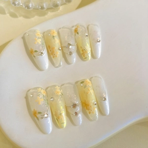 Détails d'ongles en amande avec relief floral jaune et touches de paillettes nacrées