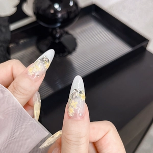 Détail d'ongles amande longs avec motifs floraux jaunes et accents de perles argentées