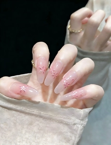 Macro detail of long almond-shaped press-on nails with pink gradient and 3D floral accents