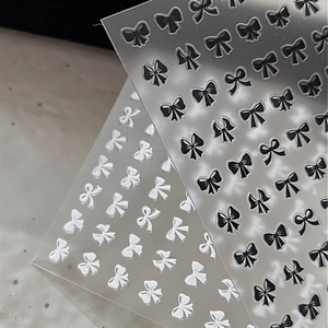 Macro shot of 3D embossed black and white bow nail stickers with detailed ribbon design