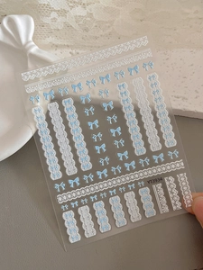 Détail d'autocollants nail art 3D avec nœuds bleus et motifs de dentelle blanche