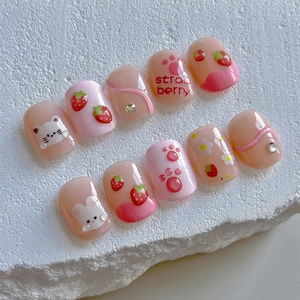 Pink cartoon press-on nails featuring strawberry, cat, and rabbit designs with rhinestones