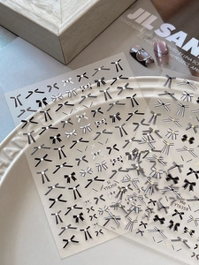 Detailed view of bow nail art stickers in black and silver on ceramic display tray