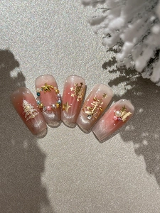 Close-up of pink cat-eye press-on nails with golden Christmas tree and 3D snowflake charms