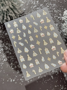 Detailed close-up of golden bronzing Christmas nail stickers with tree and snowman icons