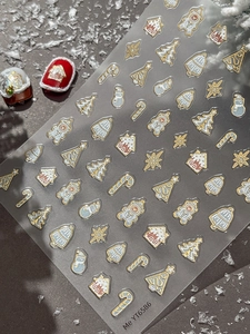 Close-up of gold Christmas nail stickers featuring gingerbread man and snow house