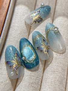 Detail of luxury press-on nails featuring blue gradient, golden butterflies and pearls