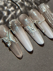 Detailed macro view of gray cat-eye nails featuring silver metal butterfly and rhinestones