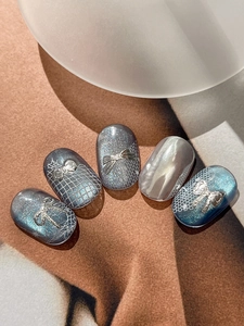 Detail of silver bow charms and laser glitter on blue-grey chic press-on nails