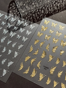 Macro detail of 3D embossed butterfly nail art stickers in metallic silver and gold tones