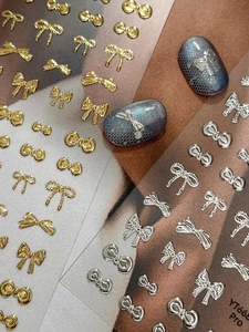 Macro shot of 3D metallic bow nail stickers in gold and silver on blue cat eye nails