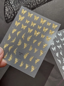 Macro shot of 3D embossed butterfly nail art stickers in shiny gold and silver tones