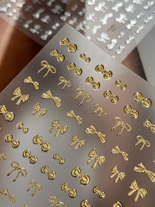 Macro shot of 3D metallic gold bow nail stickers with intricate woven texture details