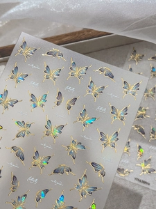 Detail of holographic blue butterfly nail stickers with gold foil outlines on silk background