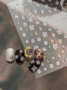 Macro detail of 3D embossed white floral nail stickers with gold outlines and Sweet time text
