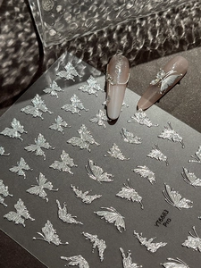 Detailed macro view of silver metallic butterfly nail decals and applied 3D decorative art