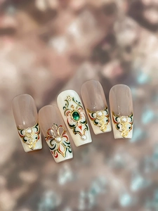Detailed macro of vintage style nail tips with gold relief and green faux gemstones