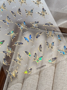Detail of holographic blue butterfly nail stickers with gold stamping and butterfly text