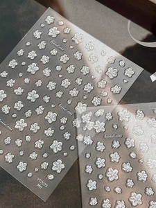 Macro detail of 3D embossed white cherry blossom nail stickers with golden outlines
