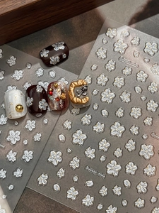 Macro detail of 3D white floral embossed nail art stickers on various manicured tips