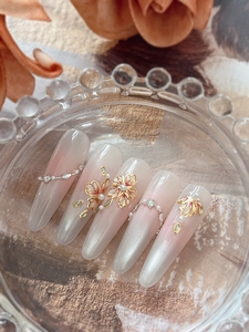 Detailed view of pink gradient press-on nails with 3D floral accents and golden outlines
