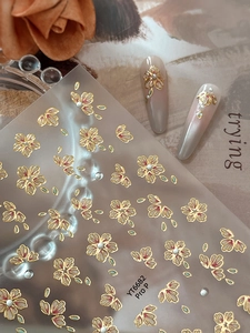 Detail showing 3D floral nail art stickers with gold foil outlines and pearl accents