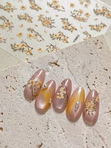Dettaglio di adesivi per unghie con fiori gialli e perle bianche su base rosa cat eye