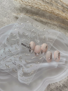 Detail view of silver leaf nail art decals on matte pink manicured nails with chic patterns