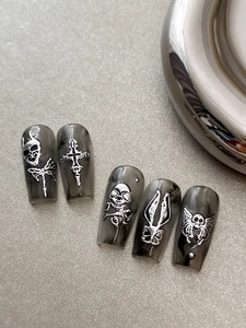 Makroaufnahme von Gothic-Nägeln mit Marmor-Muster und silbernen 3D-Totenkopf-Anhängern