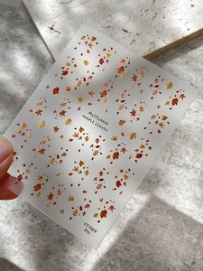 Detail of autumn maple leaf nail stickers with red and orange patterns on stone surface