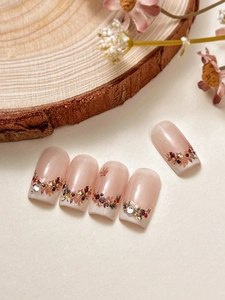 Macro detail of autumn nail art decals with pinecone, leaf designs and crystal accents