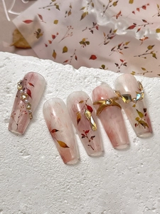 Detail of autumn leaf nail stickers with gold accents and rhinestones on long coffin nails