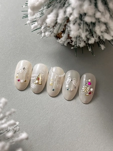 Close-up of pearl white Christmas nails with golden trees and relief bow designs
