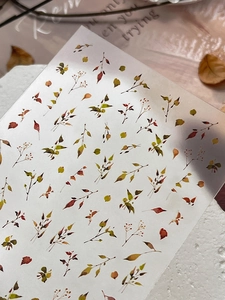 Close-up of leaf nail stickers with autumn foliage designs on a white stone background