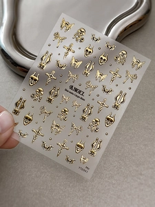 Nahaufnahme goldener 3D-Nagelaufkleber mit Totenkopf-, Kreuz- und Schmetterlingsmotiven