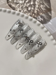 Macro detail of long coffin nails with silver cat-eye glitter and black bow-tie designs