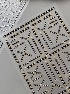 Close-up of black and gold geometric nail stickers with metallic chain patterns