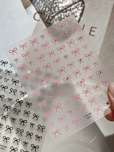 Detailed view of 3D crystal bow nail art stickers in pink and black with sparkling rhinestones