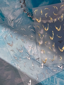 Detailed view of silver and gold 3D liquid metal nail stickers on a water wave background