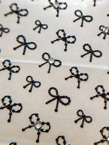 Detailed macro view of 3D black beaded bow nail stickers with rhinestone accents