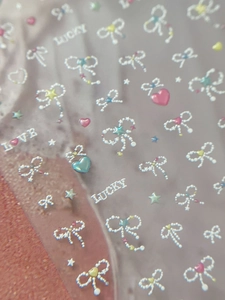 Macro detail of 3D embossed nail stickers featuring pearl bows, stars, and lucky letters