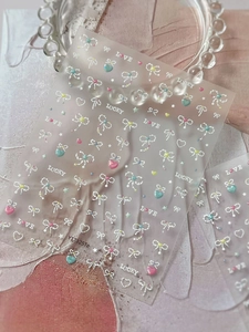 Close-up of 3D macaron nail stickers featuring pearly stars and ribbon bow accents