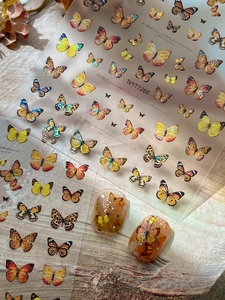 Laser butterfly nail decals with realistic gold and orange patterns on wooden background