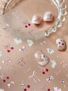 Detail of 3D nail art stickers featuring pink bows, white rabbits and sparkling rhinestones